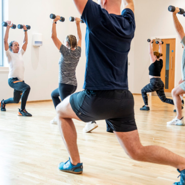 A group of people performing single leg squats while holding small dumbells above their heads